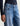 Close-up of a person wearing blue denim jeans with a faded wash and a black long-sleeve top, shown against a light neutral background.