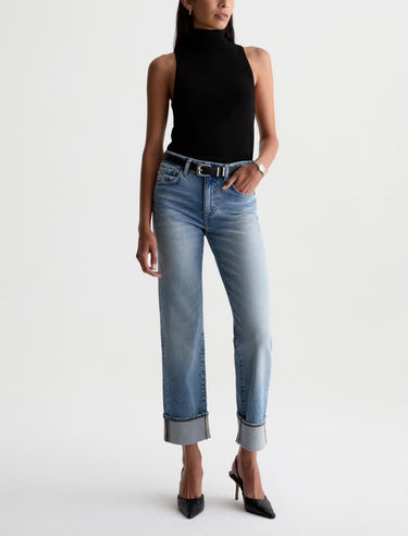 A model wearing light-wash blue cropped jeans with rolled cuffs, a black sleeveless mock-neck top, and black pointed-toe heels, photographed against a plain white studio background.
