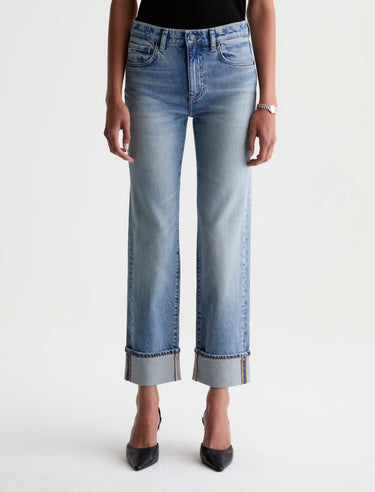 A model is shown from the waist down wearing a pair of light-wash blue cropped jeans with rolled cuffs, paired with black pointed-toe heels against a plain white studio background.