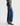 A woman wearing mid-rise medium blue wash straight leg denim with a distressed hem, fading, and gold stitching on a white background.