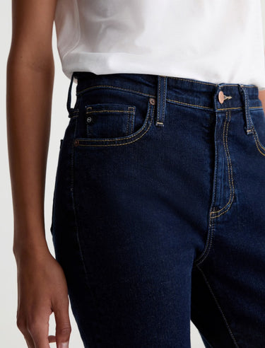 Person wearing dark blue jeans and a white shirt on a light background