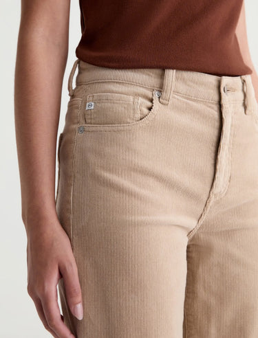 A woman wearing wide leg tan corduroy pants with a relaxed silhouette on a white background