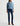 A model wearing a light blue long-sleeve knit polo-collar sweater, dark blue skinny jeans, and brown pointed-toe heeled ankle boots, standing against a plain white studio background.