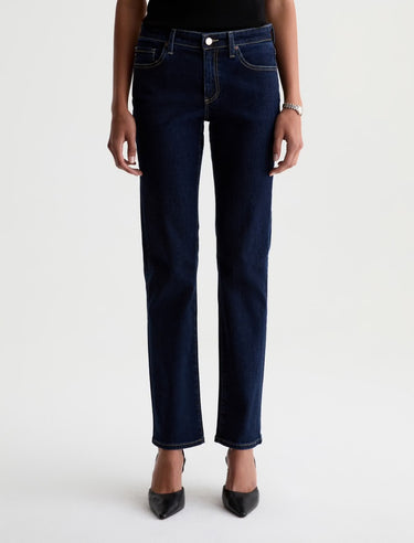 A woman wearing low rise straight dark blue jeans and black heels on a white background.