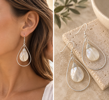 Teardrop-shaped silver dangle earrings with iridescent white mother-of-pearl drops, shown worn on a model's ear and displayed on a stone surface.