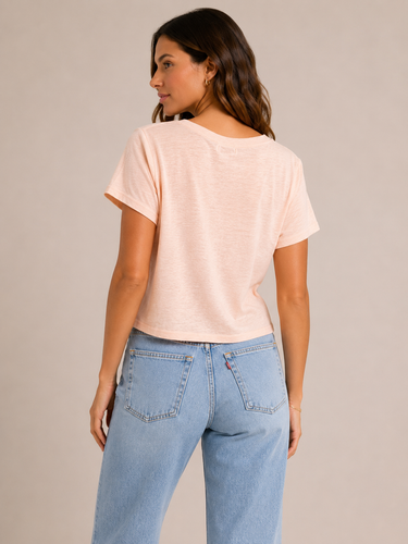 A woman wearing a light pink cropped v neck tee and jeans on a neutral background