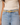 A close-up of a model wearing a light beige leather belt with a polished gold-tone buckle, styled with light-wash blue jeans and a cream ribbed tank top.