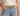 A close-up of a person wearing a light tan leather belt with a gold-tone buckle, tucked into light-wash blue jeans and a white top.