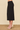 a woman wearing a black pencil midi skirt and beige heels on a neutral background