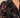 A close up of woman wearing a velvet floral mesh blouse and black jeans on a neutral background.