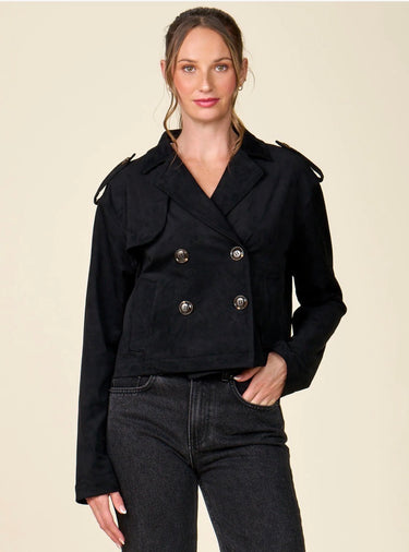 A woman modeling a black double-breasted cropped jacket with silver buttons, paired with dark black jeans, against a solid light beige background.