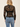 A woman wearing a long sleeve lace sheer top with a black bandeau and blue jeans on a neutral background.
