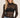 A woman wearing a long sleeve lace sheer top with a black bandeau and blue jeans on a neutral background.