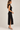 a woman wearing a black lace mock neck sleeveless dress with a side slit on a white background