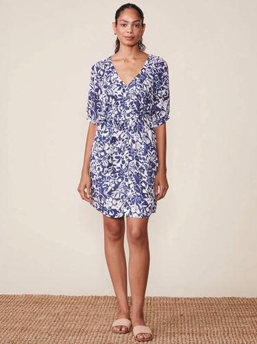 Woman wearing a blue floral dress standing on a woven mat with a beige background