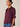 A woman wearing a short-sleeve button-up blouse in deep burgundy with ruffled cuffs, paired with blue jeans, photographed against a plain beige studio background.