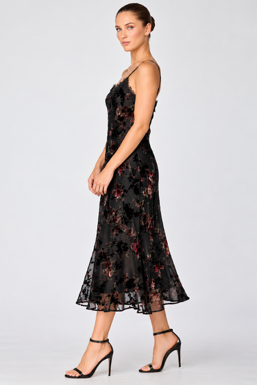 a woman wearing a black dress with lace along the neckline and colorful floral velvet detailing.