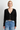 A woman wearing a black cardigan and blue jeans on a white background.