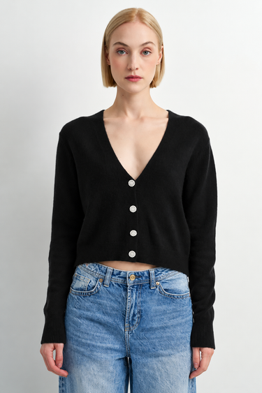 A woman wearing a black cardigan and blue jeans on a white background.