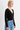 A woman wearing a black cardigan and blue jeans on a white background.