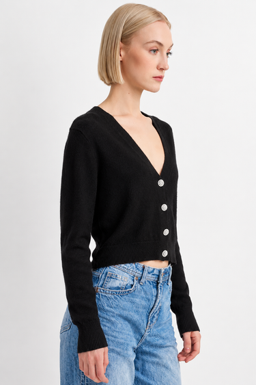 A woman wearing a black cardigan and blue jeans on a white background.