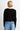 A woman wearing a black cardigan and blue jeans on a white background.