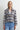 A woman wearing a blue plaid flannel jacket and blue jeans on a white background.
