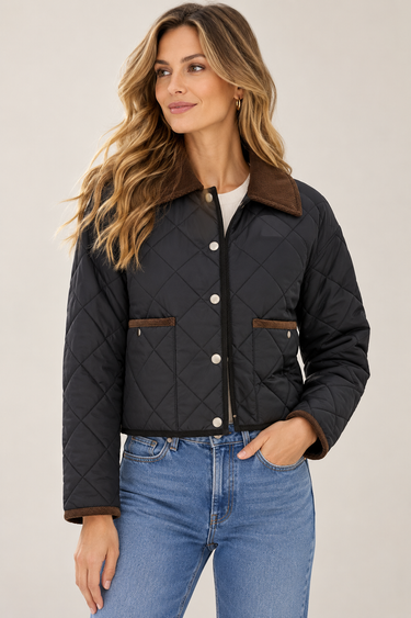 A woman wearing a black diamond-quilted jacket with a brown collar and pocket trim, paired with blue jeans, against a light beige studio background.