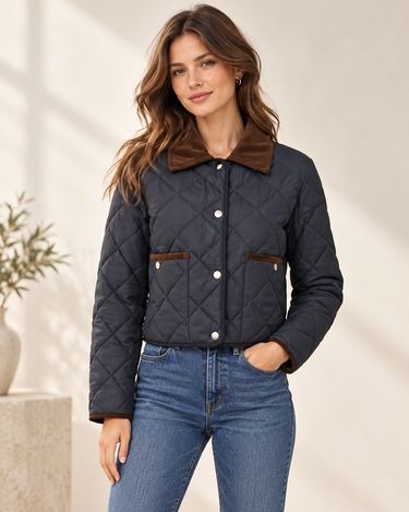 a woman wearing a black quilted jacket with front pockets lined brown corduroy and a brown corduroy collar on a neutral background.