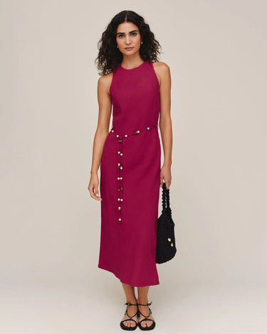 Woman wearing a sleeveless magenta dress with buttons on a plain background