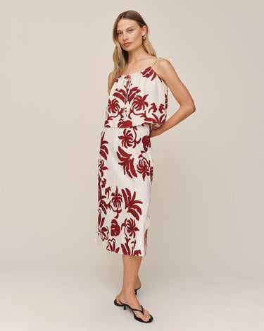 Woman wearing a white dress with red floral patterns on a plain background