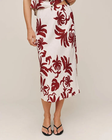 Person wearing a white skirt with red floral pattern on a plain background