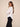 A woman posing in a white long-sleeve blouse and black wide-leg trousers against a solid beige studio background.