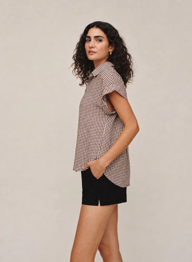 A woman wearing a brown gingham button up top and balms shorts on a white background