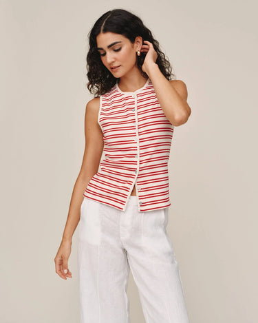 Woman wearing a red and white striped sleeveless top with white pants on a beige background