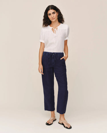 Woman wearing a white top and navy pants on a beige background