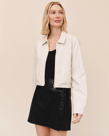 A woman wearing a black top, leather skirt, and a cropped blazer on a white background.