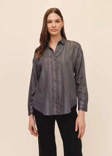 A woman wearing a smoke grey striped blouse and black jeans on a studio background.