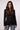 A woman wearing a black hooded blazer with a front zipper and gold-tone buttons, paired with blue jeans, against a plain light gray studio background.