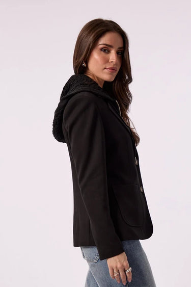 A woman modeling a black blazer over a black top with wide-leg blue jeans, standing against a light gray studio background.