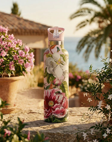 Floral-patterned water bottle on a stone ledge with plants and a building in the background