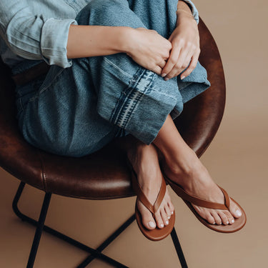 Person wearing brown sandals sitting on a brown chair with a neutral background