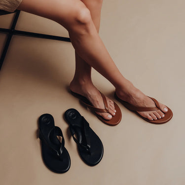 Brown sandals worn by a person with black sandals on the floor.