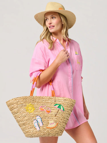 Woman in pink shirt and straw hat holding a straw bag with beach-themed decorations on a white background