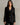a woman wearing a black blazer with gold button accents and black pants with a white stripe on a neutral background