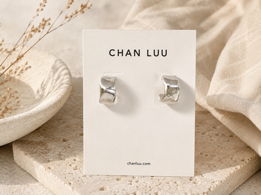 A pair of hammered cuff silver hoops on a branded ‘Chan Luu’ cardstock on an aesthetic background