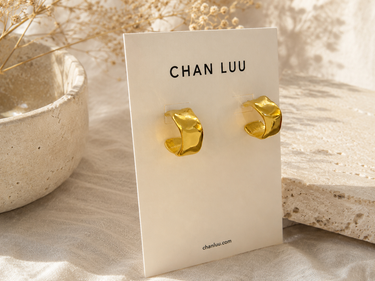 Textured gold cuff hoop earrings on branded cardstock on a neutral background.