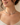 A close-up of a woman wearing a delicate multi-colored gemstone choker necklace with a gold chain, set against a soft beige background.