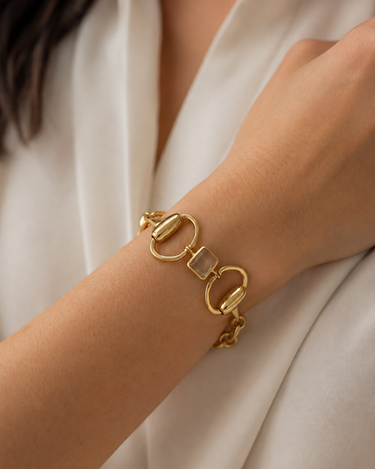 A gold horsebit chain bracelet with a clear square-cut gemstone in the center