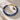 A beaded bracelet made of polished blue round beads with a gold-tone clasp and two charms, one heart-shaped and one teardrop-shaped dark blue stone, displayed on a textured beige stone surface.